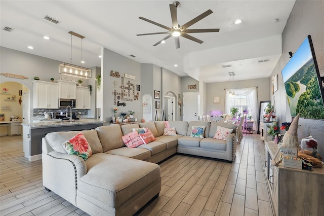 living area with a ceiling fan, wood finish floors, arched walkways, and visible vents