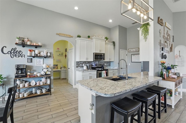 kitchen featuring backsplash, a sink, white cabinetry, stainless steel appliances, and arched walkways