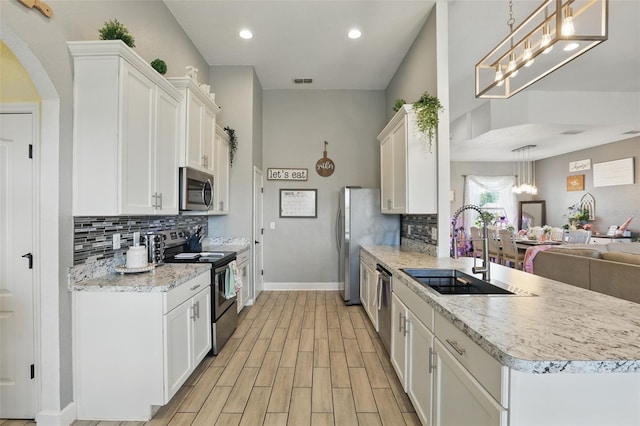 kitchen featuring open floor plan, white cabinetry, stainless steel appliances, a sink, and light wood-style flooring
