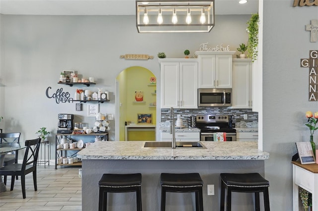 kitchen with a sink, white cabinetry, tasteful backsplash, a breakfast bar, and stainless steel appliances