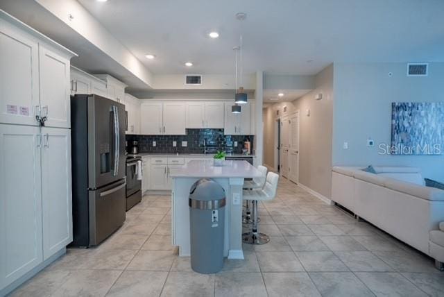 kitchen featuring open floor plan, a kitchen bar, stainless steel fridge with ice dispenser, range, and visible vents