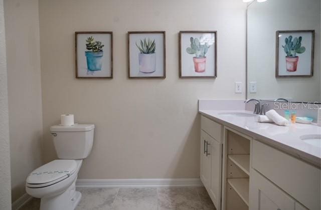 bathroom featuring double vanity, toilet, baseboards, and a sink