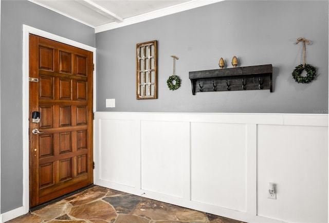 foyer entrance with crown molding, a decorative wall, stone finish flooring, and a wainscoted wall