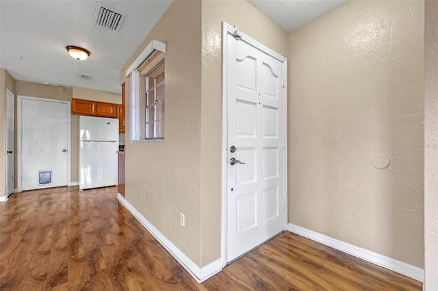 entryway featuring baseboards, visible vents, wood finished floors, and a textured wall
