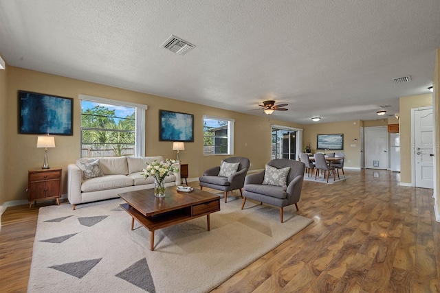 living room with a ceiling fan, wood finished floors, a textured ceiling, and visible vents