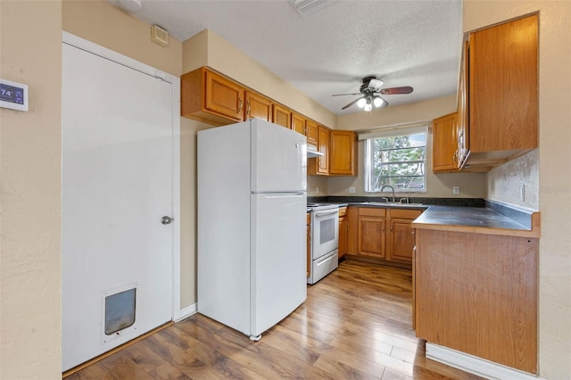 kitchen with a textured ceiling, light wood-type flooring, white appliances, dark countertops, and ceiling fan