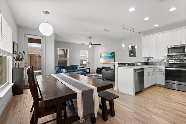 kitchen with white cabinets, a peninsula, a sink, decorative backsplash, and appliances with stainless steel finishes