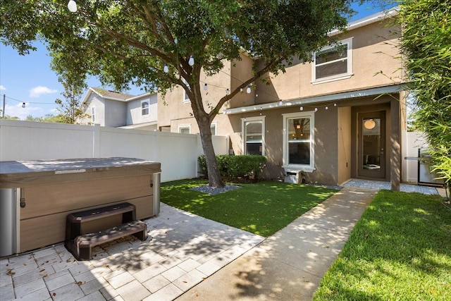 view of front of property featuring fence, a front lawn, stucco siding, a patio, and a hot tub
