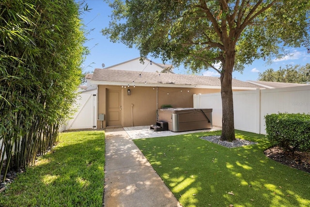 exterior space featuring a gate, fence, a hot tub, a front yard, and stucco siding