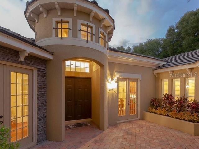 property entrance featuring stone siding, stucco siding, and french doors