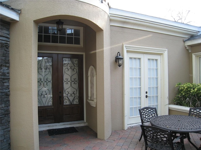 view of exterior entry featuring outdoor dining area, stucco siding, french doors, and a patio area