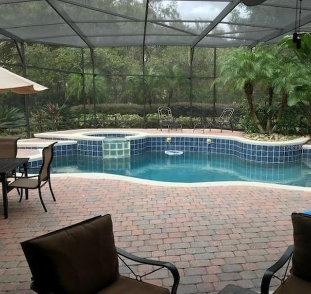 view of pool with a patio area, glass enclosure, and a pool with connected hot tub