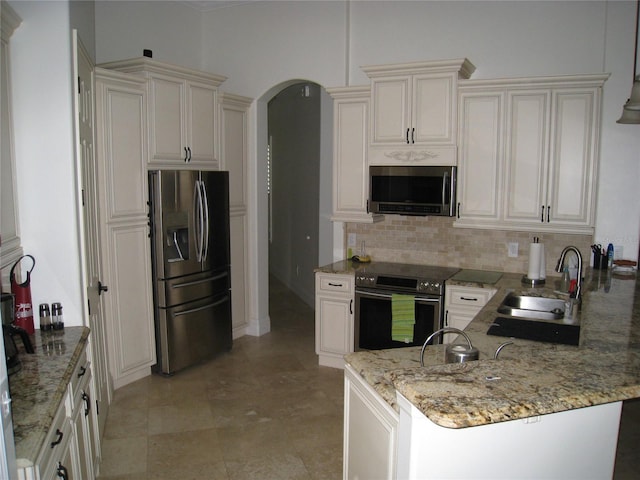 kitchen featuring light stone countertops, a sink, arched walkways, backsplash, and stainless steel appliances