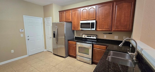 kitchen featuring baseboards, stainless steel appliances, dark stone countertops, a sink, and light tile patterned floors
