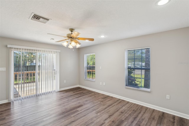 empty room featuring a wealth of natural light, visible vents, and wood finished floors