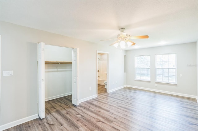 unfurnished bedroom featuring a closet, a ceiling fan, wood finished floors, a walk in closet, and baseboards