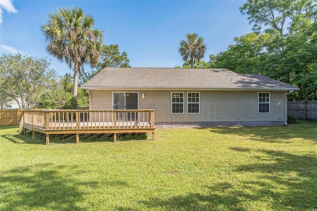back of property featuring a yard, a deck, fence, and a shingled roof