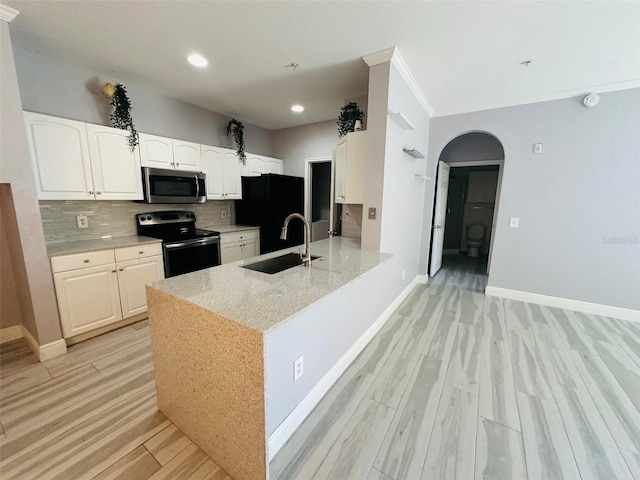 kitchen with tasteful backsplash, arched walkways, a sink, light wood-style floors, and black appliances