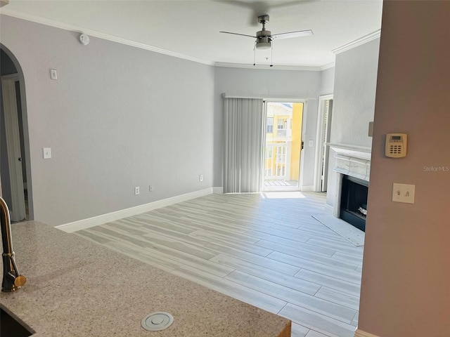 unfurnished living room with arched walkways, light wood-type flooring, a ceiling fan, a fireplace, and crown molding