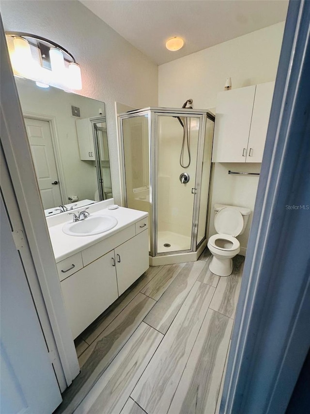 full bathroom with vanity, wood finish floors, a textured wall, toilet, and a shower stall