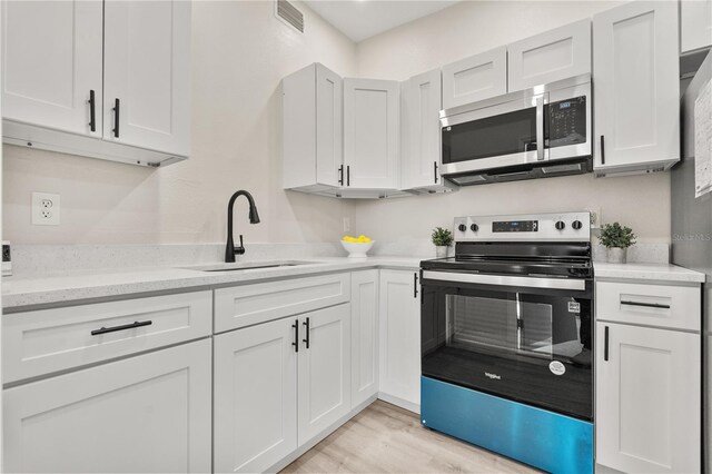 101 W Wallace St, Orlando, FL 32809 - kitchen featuring light wood-type flooring, a sink, visible vents, white cabinets, and appliances with stainless steel finishes