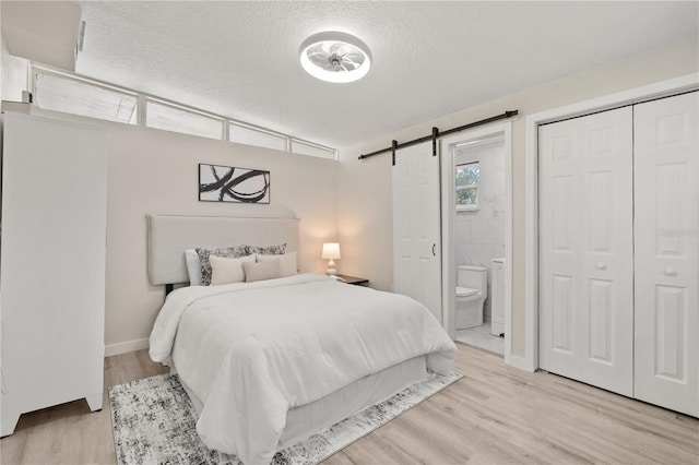 101 W Wallace St, Orlando, FL 32809 - bedroom featuring connected bathroom, a closet, a barn door, a textured ceiling, and light wood-style flooring