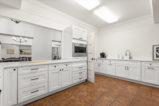 kitchen with stainless steel microwave, a sink, an inviting chandelier, crown molding, and light countertops
