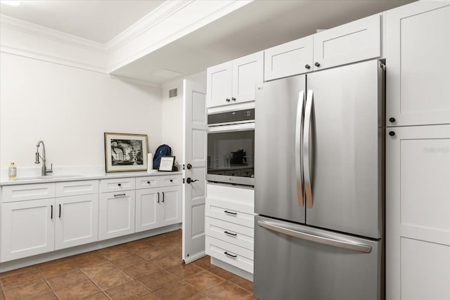 kitchen with stainless steel appliances, white cabinets, ornamental molding, a sink, and visible vents