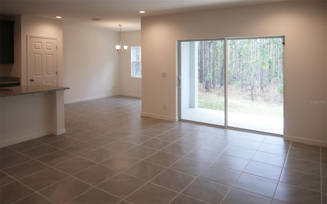 unfurnished living room featuring baseboards, dark tile patterned floors, recessed lighting, and a chandelier