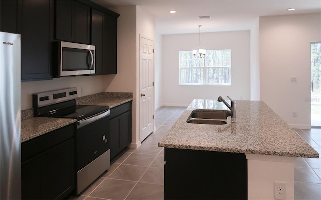 kitchen with a notable chandelier, a sink, appliances with stainless steel finishes, tile patterned flooring, and a kitchen island with sink