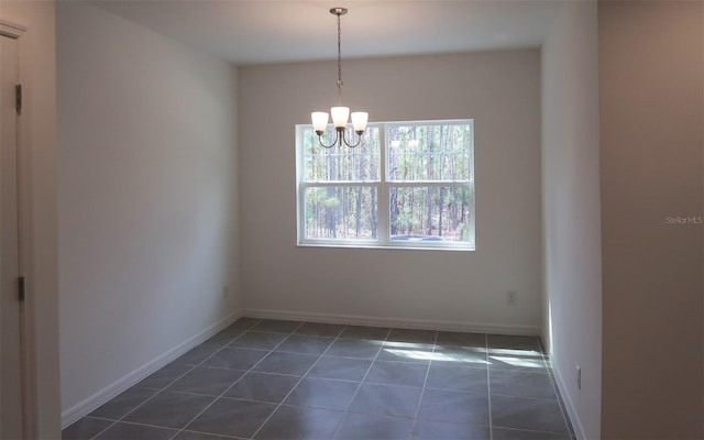 empty room featuring baseboards, dark tile patterned floors, and a chandelier