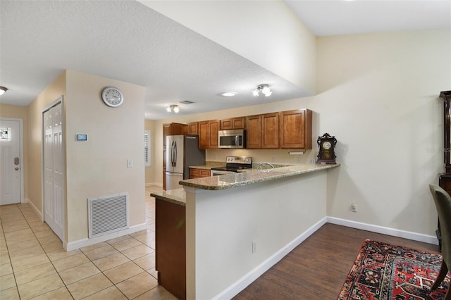 1034 Weathered Wood Cir, Winter Springs, FL 32708 - kitchen with appliances with stainless steel finishes, brown cabinetry, a peninsula, baseboards, and light stone counters