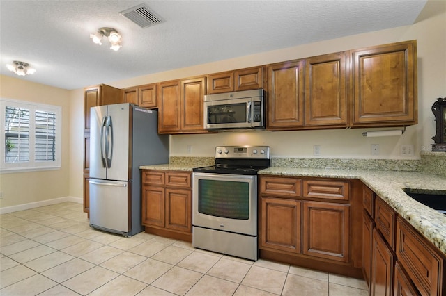 1034 Weathered Wood Cir, Winter Springs, FL 32708 - kitchen with appliances with stainless steel finishes, brown cabinets, light stone countertops, a textured ceiling, and light tile patterned flooring
