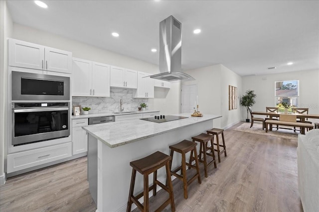 kitchen with a sink, a breakfast bar, island exhaust hood, white cabinets, and appliances with stainless steel finishes