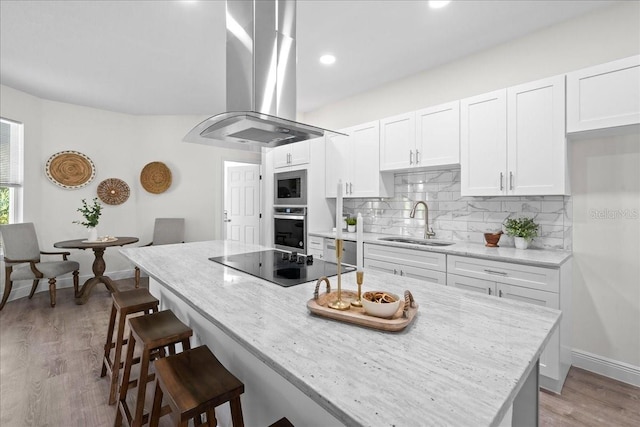 kitchen featuring white cabinets, stainless steel appliances, island range hood, a sink, and light stone countertops