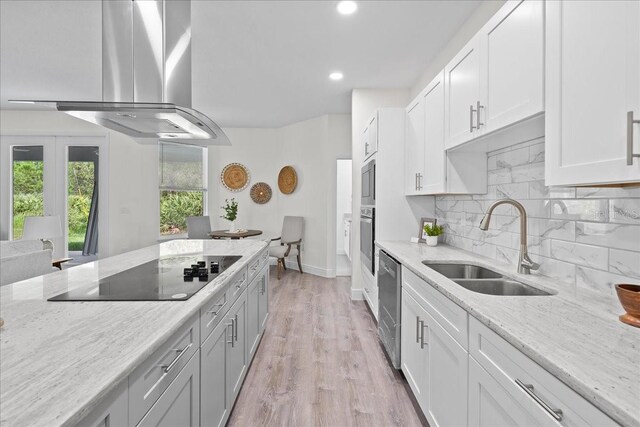 kitchen with island exhaust hood, a sink, backsplash, light stone counters, and appliances with stainless steel finishes