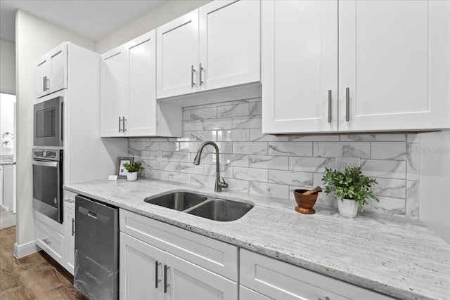 kitchen with stainless steel appliances, backsplash, a sink, light stone countertops, and white cabinetry