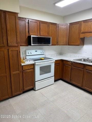 kitchen featuring white range with electric stovetop, light countertops, stainless steel microwave, and brown cabinetry