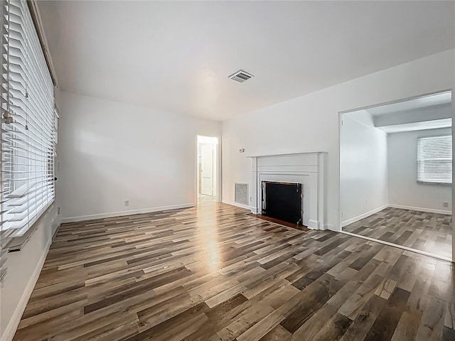 unfurnished living room with wood finished floors, a fireplace with flush hearth, and baseboards