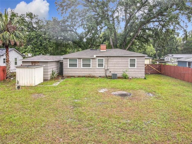 back of house with a storage shed, a chimney, an outbuilding, roof with shingles, and central air condition unit