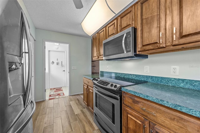 2436 Deer Trail Ln, Spring Hill, FL 34606 - kitchen with stainless steel appliances, brown cabinetry, light wood-style flooring, dark countertops, and a textured ceiling
