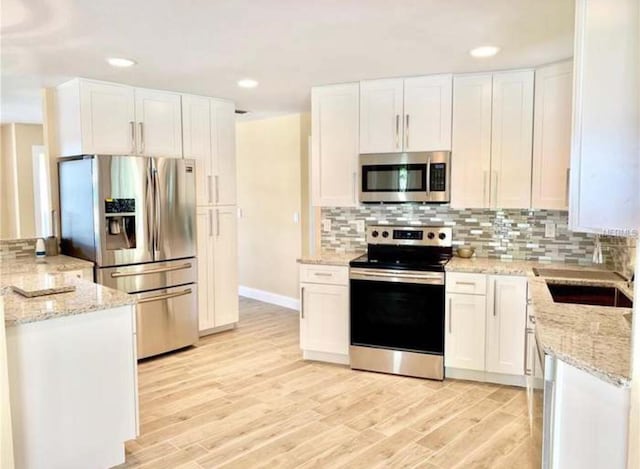 kitchen featuring stainless steel appliances, tasteful backsplash, light wood-type flooring, white cabinetry, and light stone counters