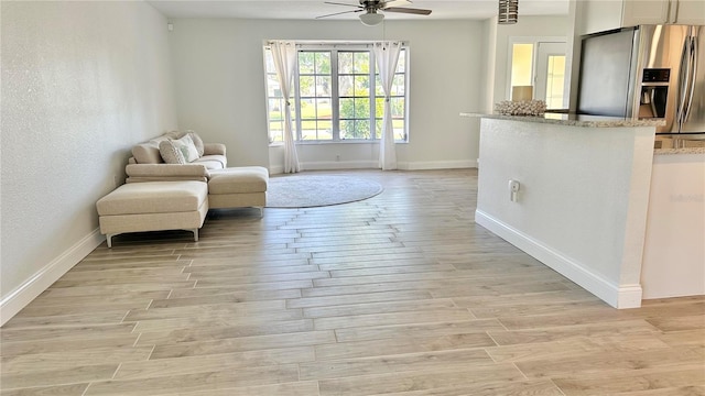 living area with a ceiling fan, baseboards, and light wood-style floors