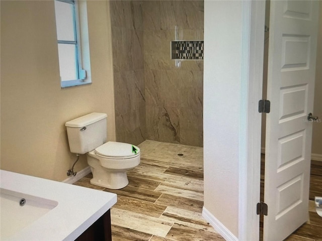 full bath with toilet, tiled shower, vanity, and baseboards