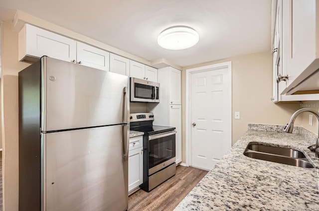 kitchen with light stone counters, appliances with stainless steel finishes, a sink, white cabinetry, and wood finished floors
