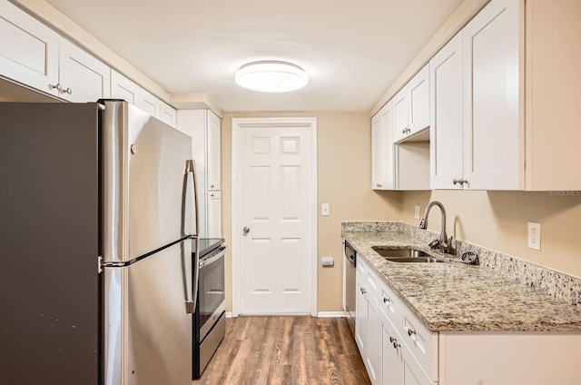 kitchen with wood finished floors, light stone countertops, white cabinetry, a sink, and appliances with stainless steel finishes