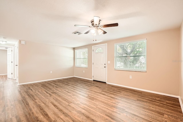 spare room featuring plenty of natural light, ceiling fan, wood finished floors, and visible vents