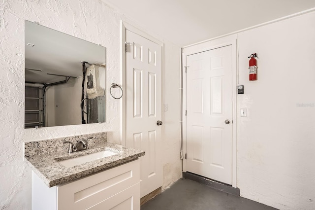 bathroom with vanity, concrete floors, and a textured wall