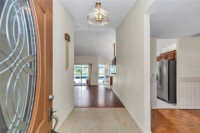 entrance foyer with a textured ceiling, visible vents, a chandelier, baseboards, and lofted ceiling