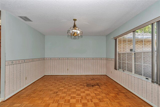 spare room with wainscoting, visible vents, a chandelier, and a textured ceiling